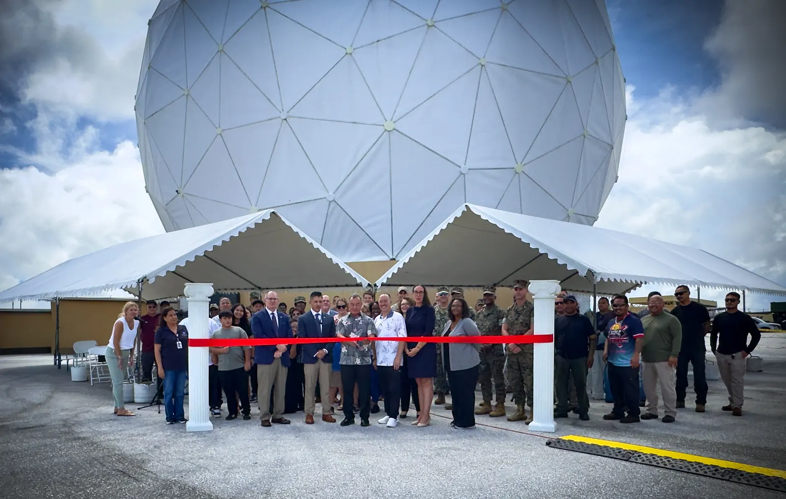 A group cuts a red ribbon in front of the large white antenna dome at NASA’s Guam station.