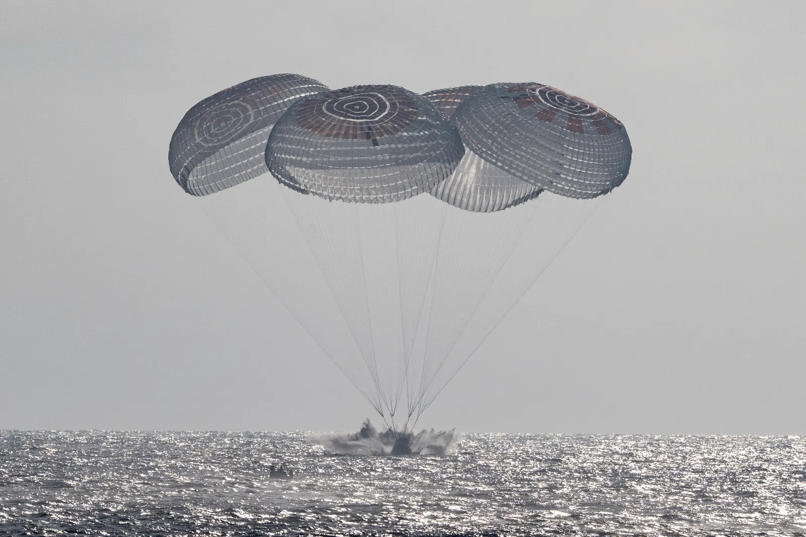 The Freedom capsule touches the ocean beneath four parachutes