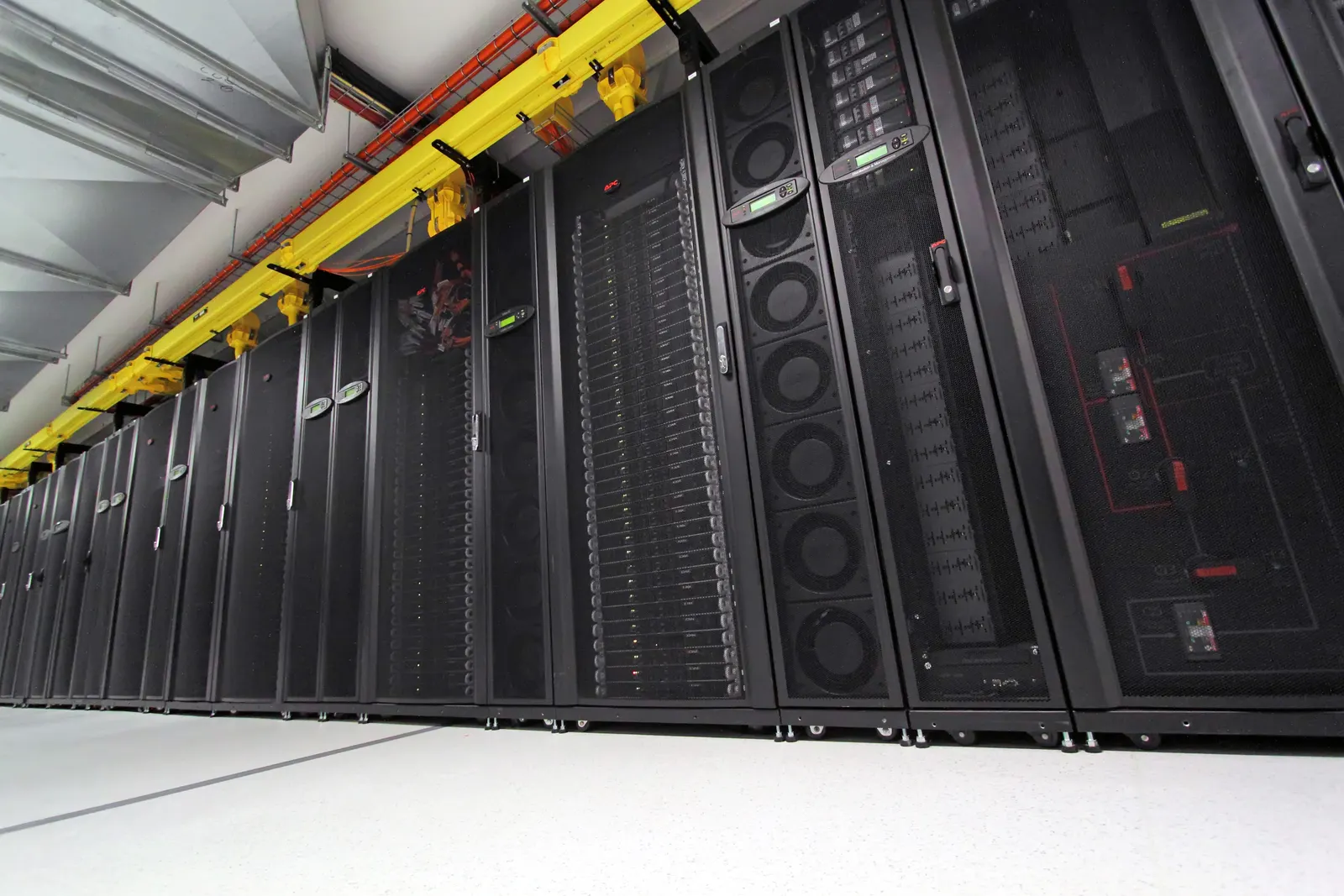 A row of black computer racks containing servers, with yellow cables overhead.