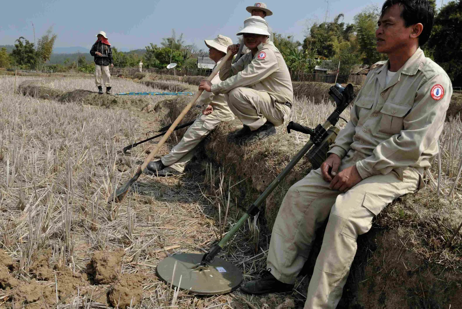 Members of an ordnance-clearance team resting in a field in Laos with metal detectors