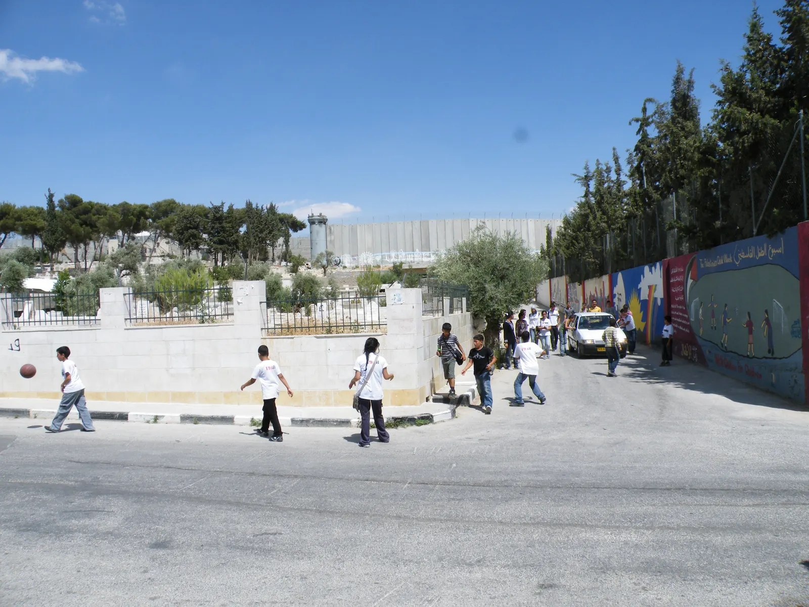 Children walk and play in a street near Aida Camp, with a wall in the background.