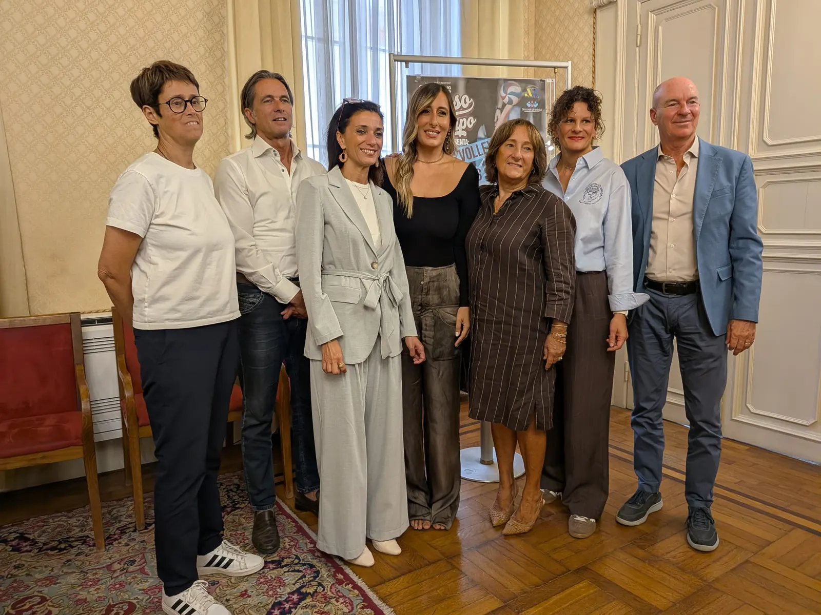 Participants at the Stesso Campo presentation pose in front of the project poster in a council room.
