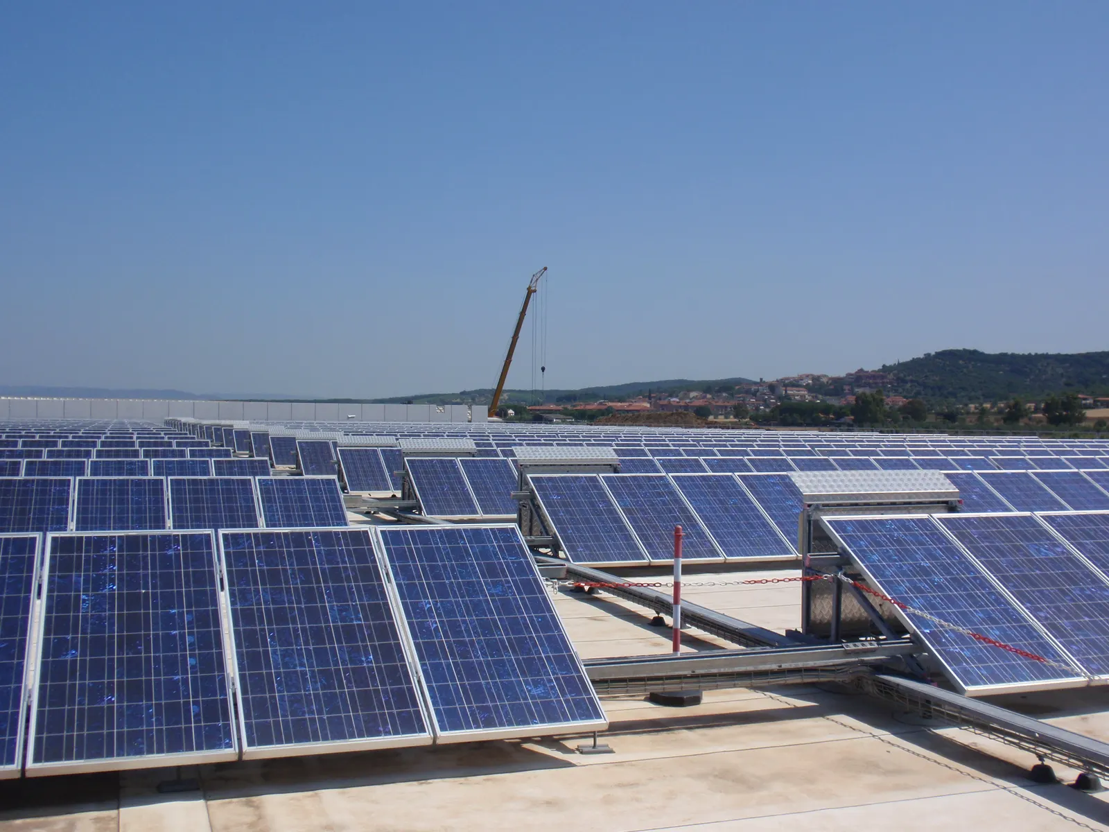Rows of tilted solar panels on a building’s roof, with hills in the background.