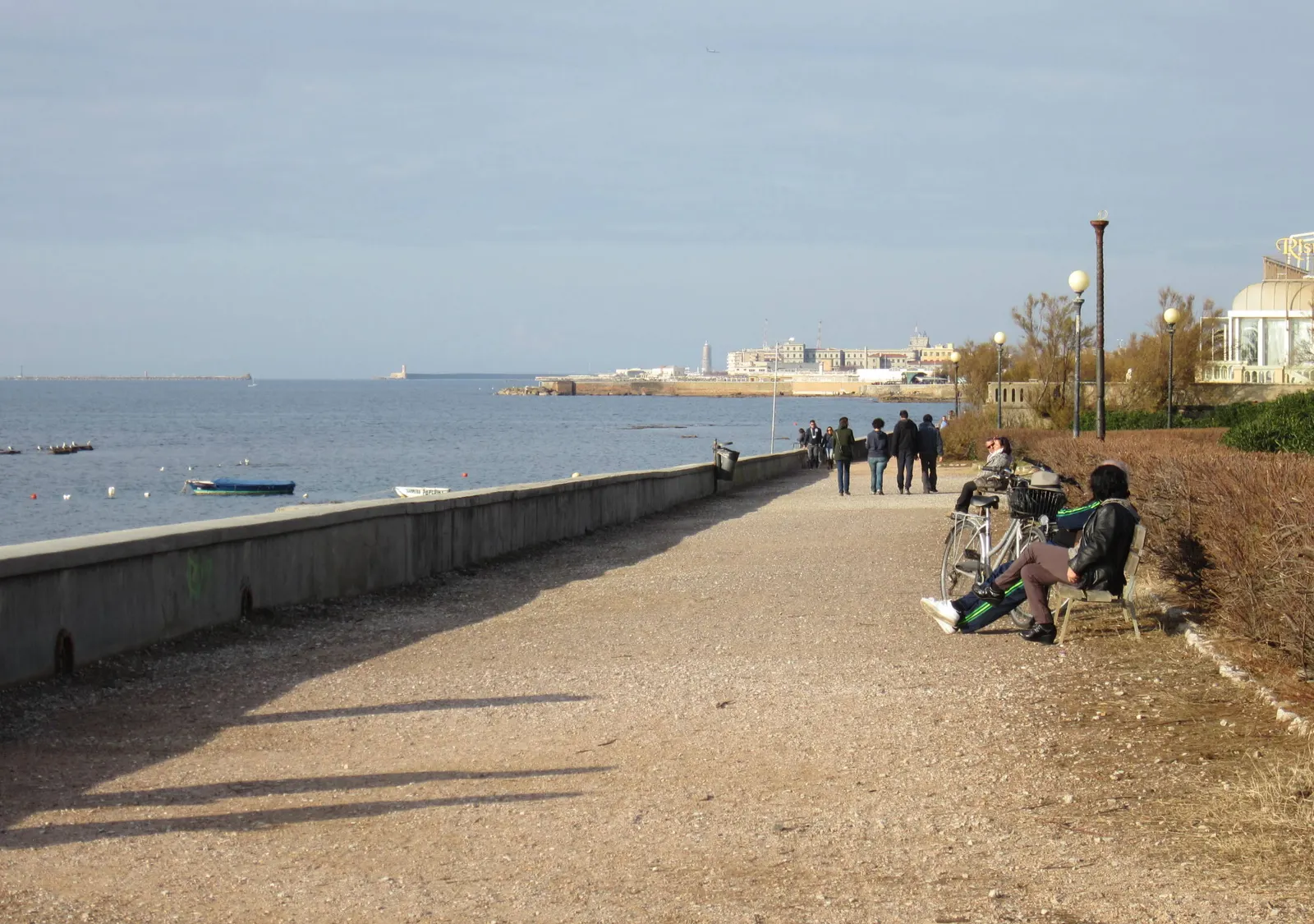 The seafront promenade in Antignano, with people walking, benches and bicycles.