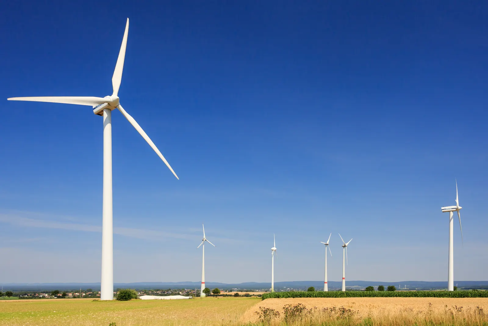 White wind turbines among fields in Paderborn, beneath a blue sky.