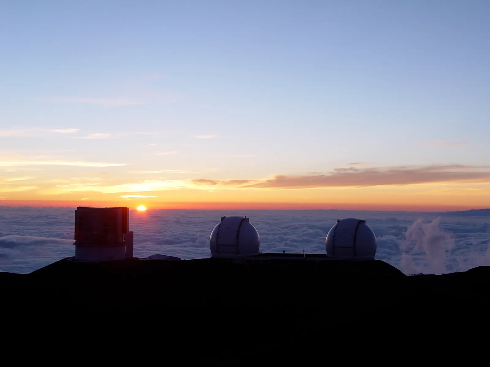 The Subaru and Keck telescope buildings at sunset, above the clouds.