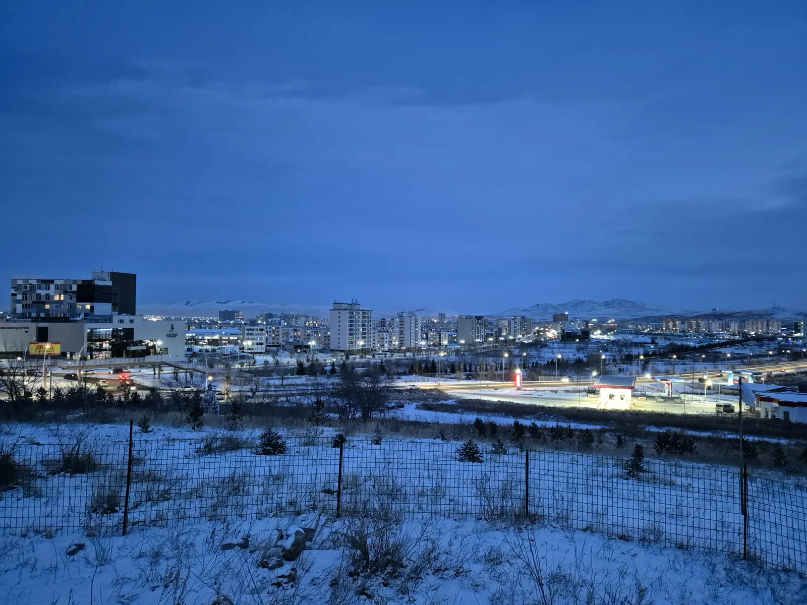 Buildings and roads in Darkhan at dusk, with snow and hills in the background