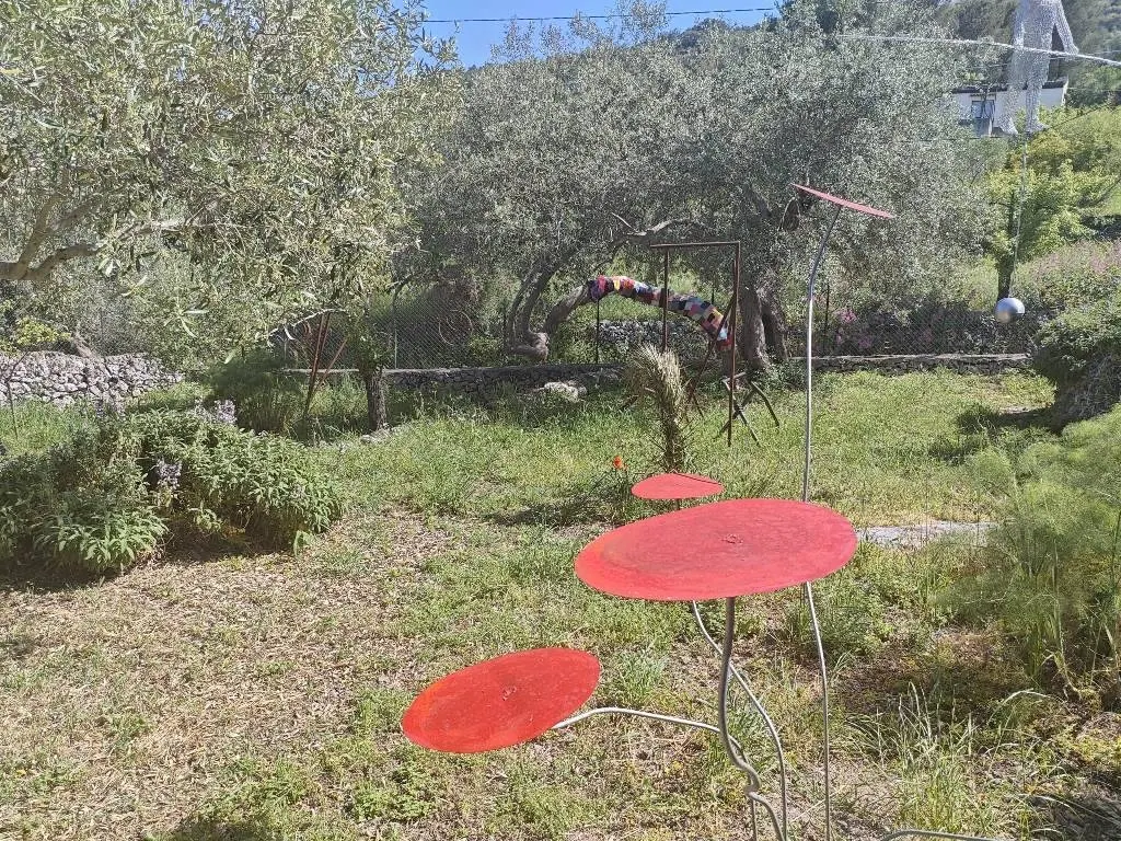 Sculptures with red discs and other metal forms among olive trees at Giardino Bianco park