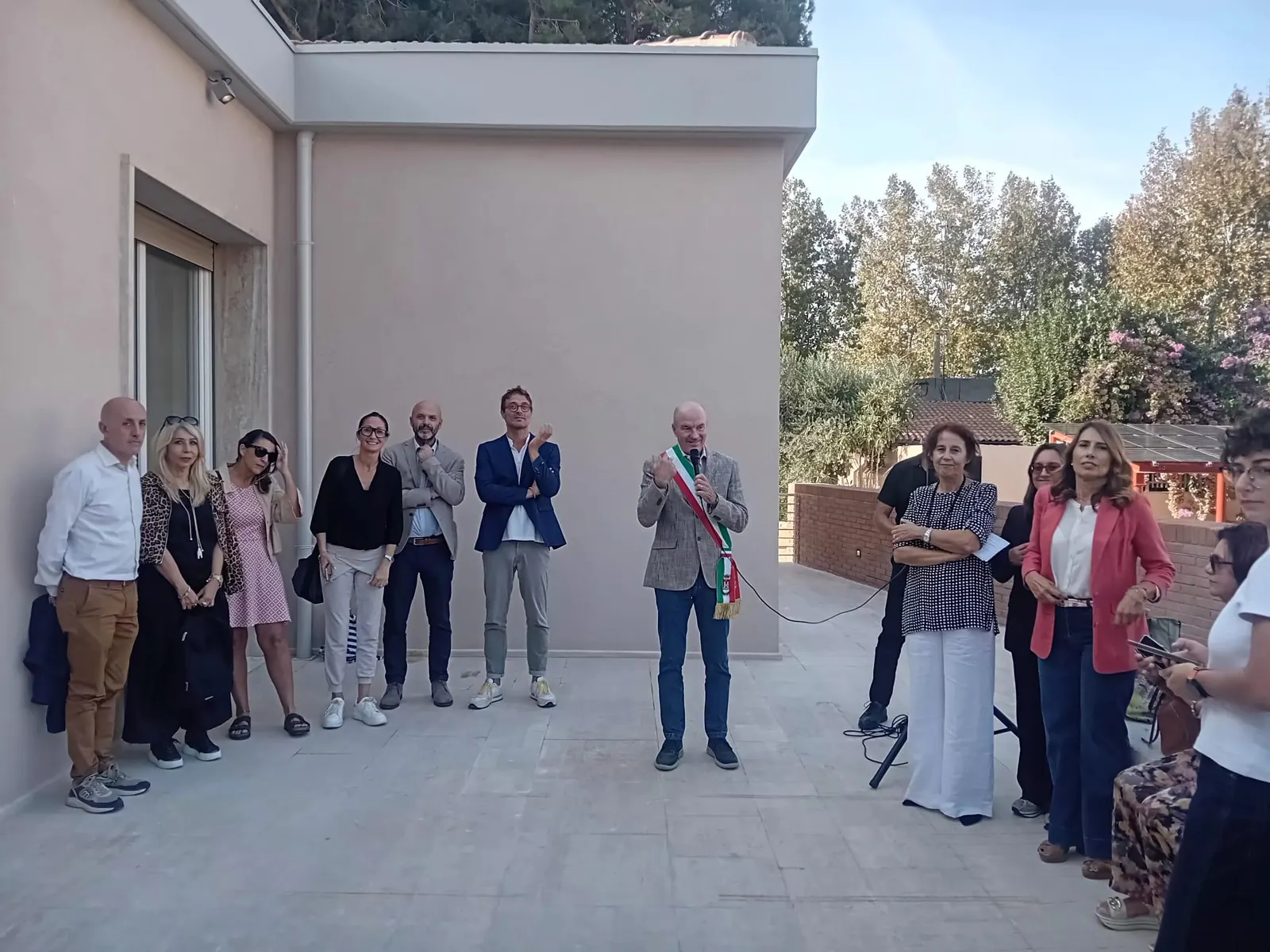 Participants outside the La Trottola centre during its opening, with a speaker using a microphone.