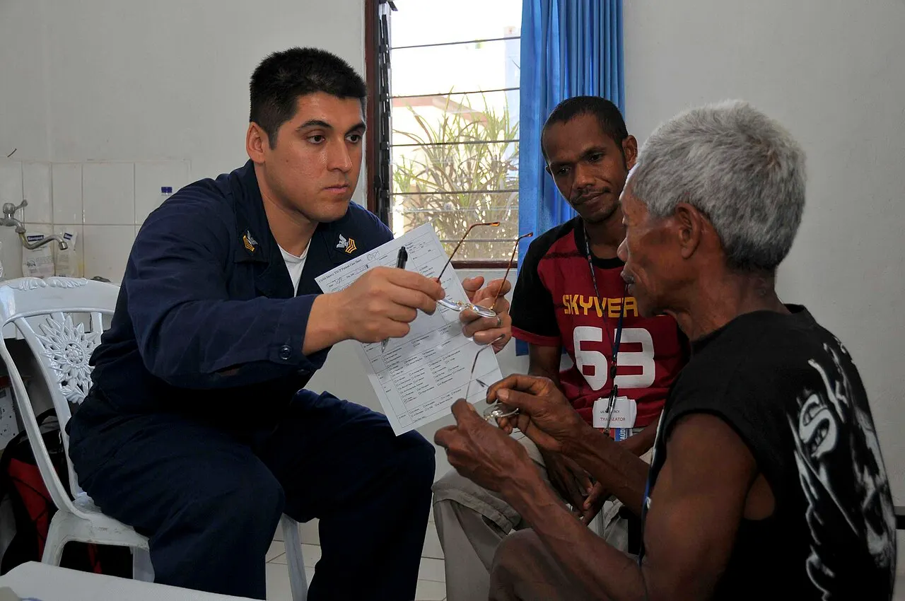 A healthcare worker carries out an eye examination with an older man and an interpreter.