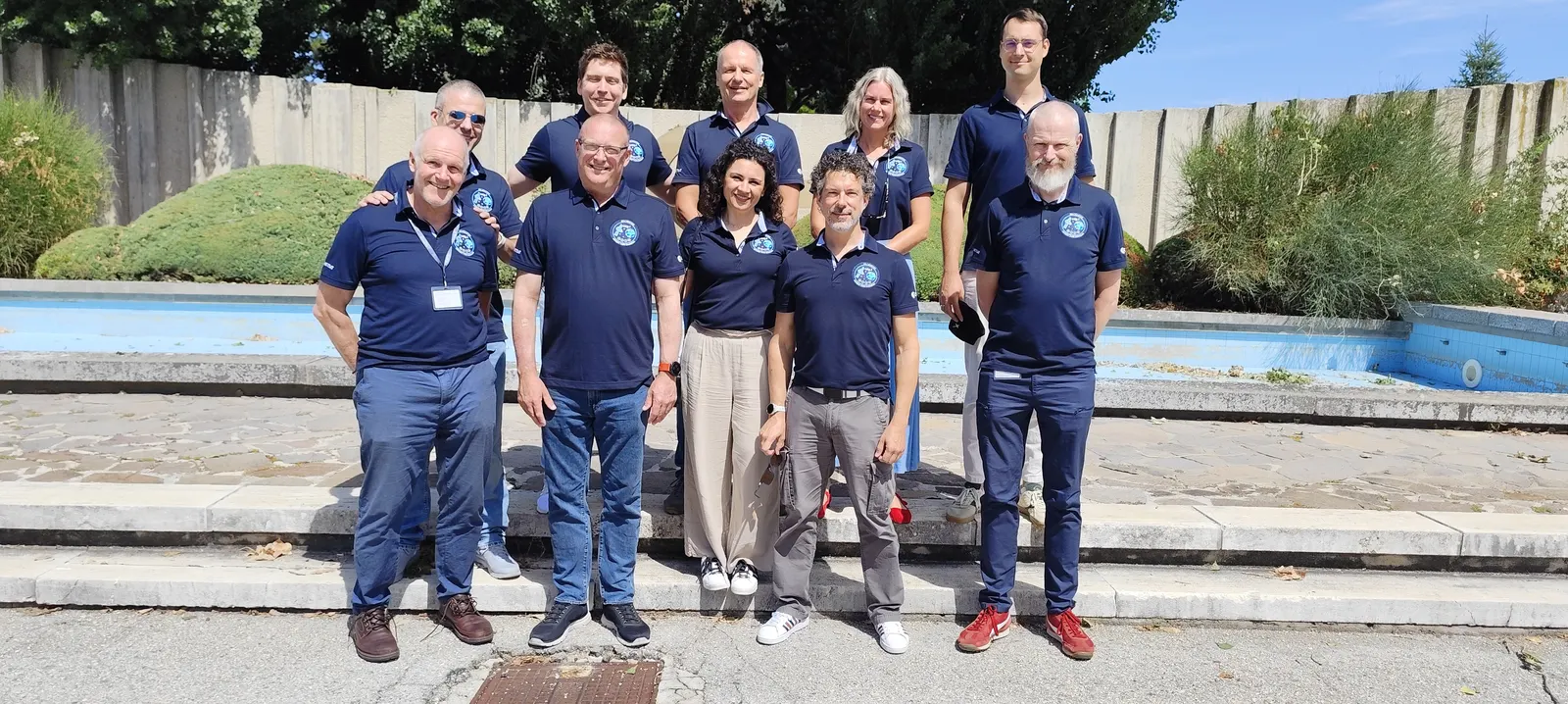 Members of ESA’s MTG-I2 team pose outdoors in blue polo shirts in front of a basin.